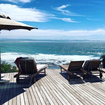 Three Sun loungers and a parasol on a wooden deck overlooking the ocean, Plettenberg Bay, Cape, South Africa