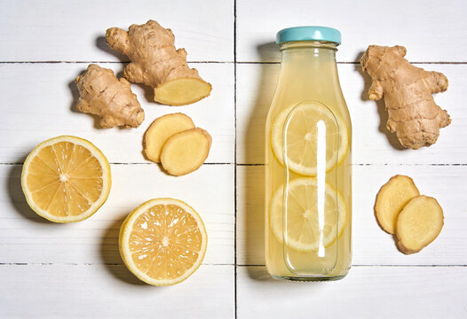 Fresh ginger root and lemon halves with homemade lemonade on white wood surface