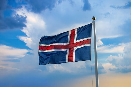 An Icelandic national flag waves in the wind under a cloudy sky.