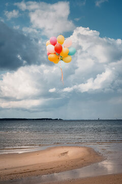 A bunch of colorful, released balloons floats above a beach on the Baltic Sea.