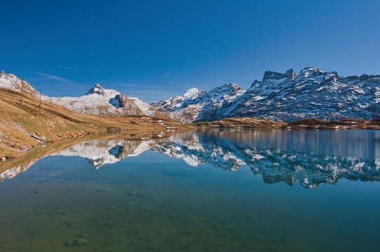 View into land of Snowcapped Swiss Alps mountain peaks reflected in Lake Tannensee in Melchsee-Frutt, Obwalden, Switzerland
