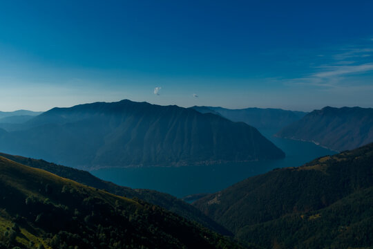 Aerial view of Lake Como surrounded by steep green mountain peaks of the Lombard Prealps, Italy