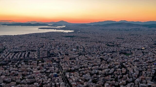 Aerial hyperlapse sunset to dusk view of the urban skyline of Athens, Attica, Greece, with soft sunlight and street and sea traffic