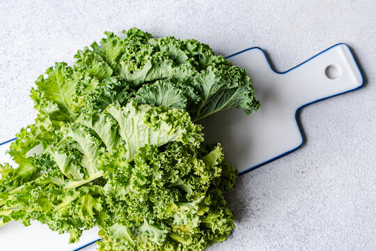 Overhead view of a fresh bunch of green curly kale leaves on a minimalist white ceramic serving platter against a textured grey background