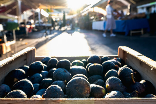 Ripe kiwis in a wooden crate at Cours Saleya food market in Nice, France, illuminated by warm morning Mediterranean sunlight, with market stalls and shoppers in the background