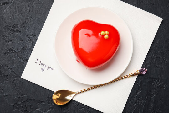 Napkin with phrase I Love You, dessert in shape of heart and spoon on black table, top view