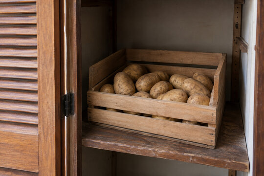 Potatoes in a slatted wooden bin inside a shaded cupboard with a louvered door