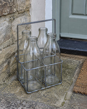 Empty glass milk bottles in a wire carrier beside a doorstep for return collection