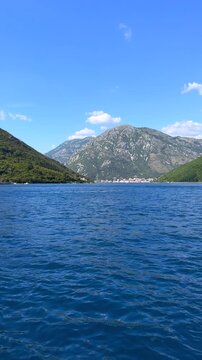 Scenic Mountain Bay with Coastal Village and Blue Sea. Scenic view across deep blue sea toward a small coastal village surrounded by green mountains under a clear summer sky.