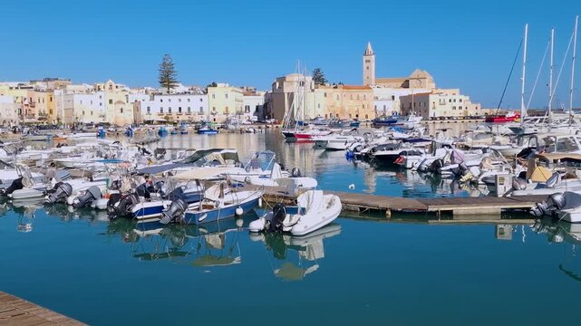 Trani marina wide angle view of yacht masts framing cathedral, tracking pan left to right, Puglia, Italy. Handheld 4K establishing B-roll, copy space sky