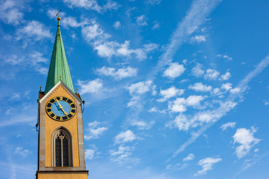Historic church clock tower with green spire under bright blue sky with light white clouds and copy space