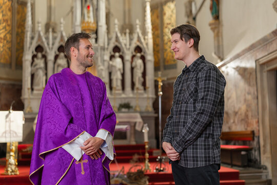 A young man student has a conversation with a catholic priest about christian faith in a church setting.