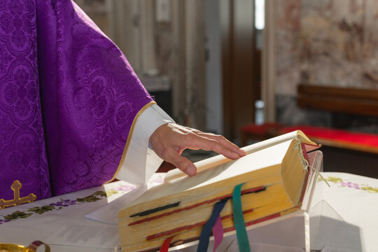 A parish priest leads a eucharistic celebration at a catholic church. The setting is focused on the priests hand on the mass book.