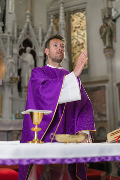 A catholic priest leads holy mass in a church, wearing liturgical vestments. One person participates in the religious ceremony.