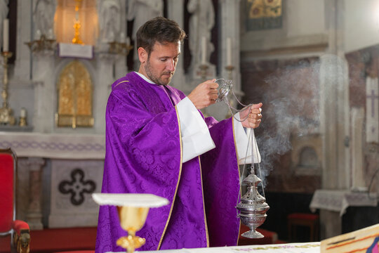 A catholic priest performs a eucharistic celebration during holy mass inside a church. Smoke rises from the incense burner.