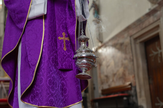 A catholic priest conducts holy mass in a church while holding a censer with incense. This ceremony is part of the eucharistic celebration.