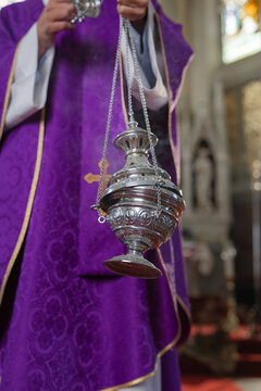 A catholic priest performs a eucharistic celebration in a church, using incense to enhance worship and devotion.
