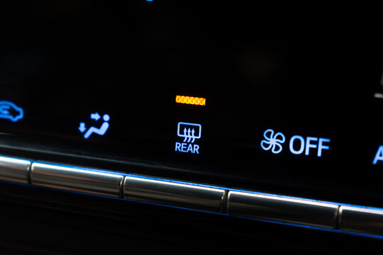 Close-up active rear window defogger defroster button with illuminated orange indicator on car dashboard.