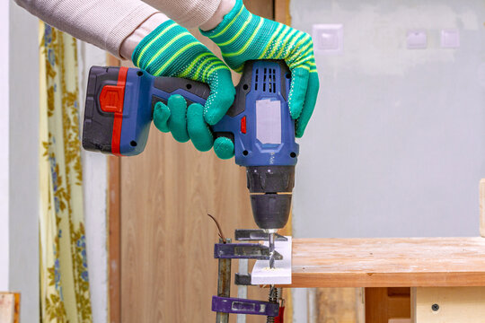 Gloved hands drill into a clamped wooden board with cordless power drill. DIY woodworking and home repair. Carpentry workshop. Practical tool use, maintenance and construction