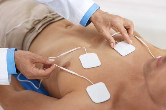 Doctor attaching ECG electrodes to patient's chest in clinic, closeup