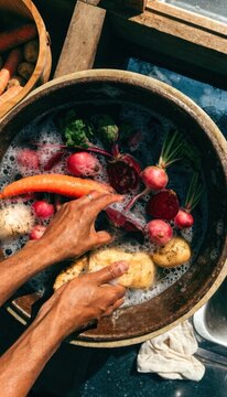 Wash vegetables and fruits for healthy eating concept. Hands washing fresh vegetables including carrots, radishes, and potatoes in a large basin filled with water.