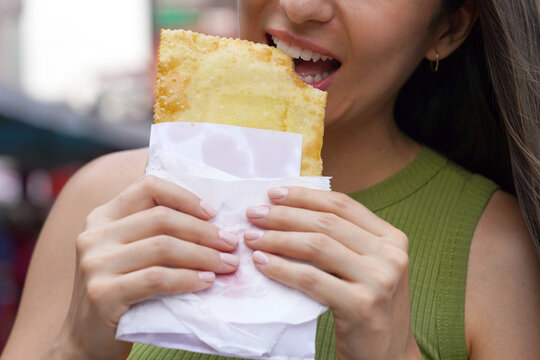 Unrecognizable woman eating Pastel de feira a typical Brazilian stuffed fried pastry