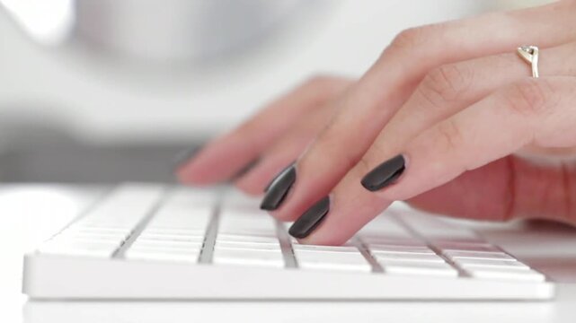 Close up of a woman with black nail polish typing on a white computer keyboard with dark fingernails typing video close