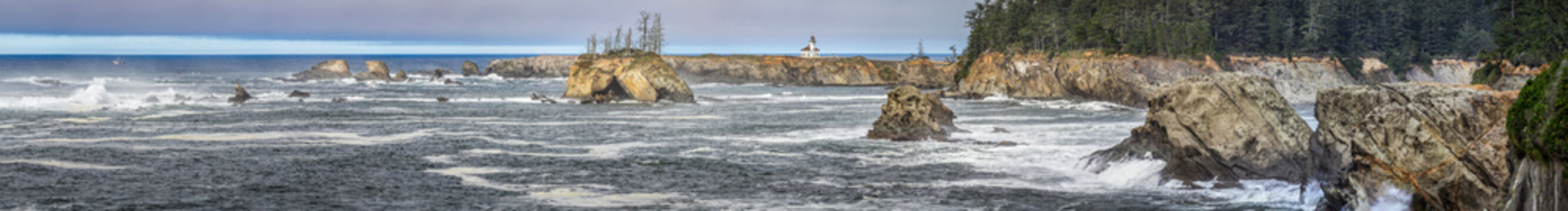 Beautiful wide panoramic view of a historic lighthouse on a wild rocky ocean coast with a distant ship