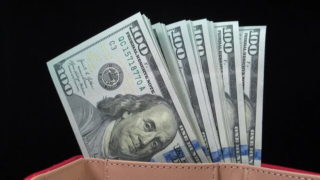 Stack of new blue hundred dollar bills in a wallet rotating against a black background, highlighting cash, personal finance, savings, and wealth