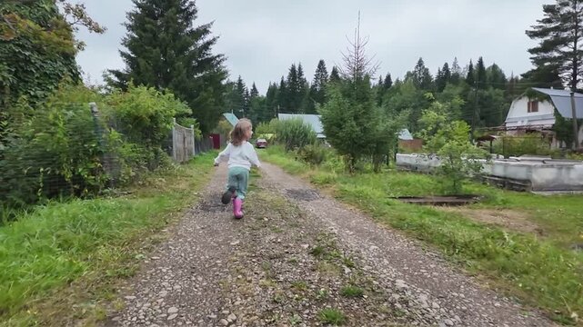 Slow motion. A child, a five-year-old girl, runs along a road on a summer day in a village.