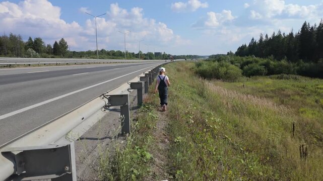A child, a five-year-old girl, walks along the side of the highway.