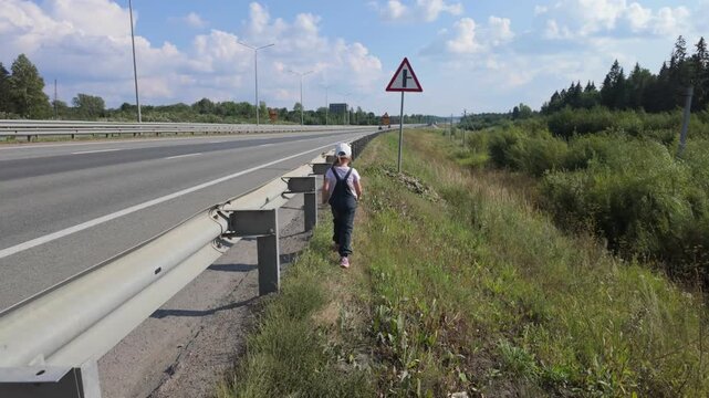 A child, a five-year-old girl, walks along the side of the highway.