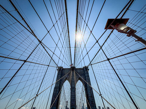 Sun shining through the cables of the Brooklyn Bridge beside a cast iron lamp post, New York, United States