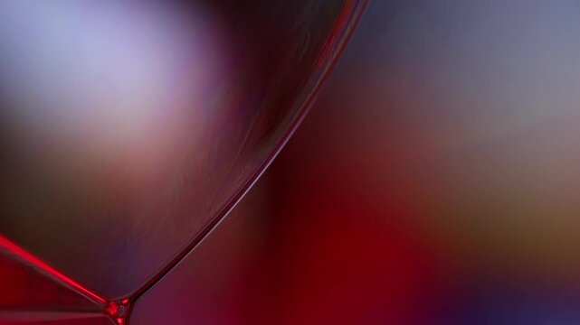 Curved crimson and violet liquid film boundary with geometric Plateau junction. A low-key macro photograph capturing a subtle liquid film membrane in deep crimson red.