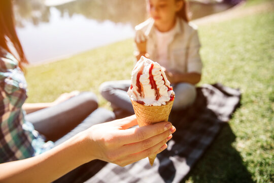 Nice picture of adult holding con of ice cream in hand. There is a girl sitting besides adult and holding con of icream too.