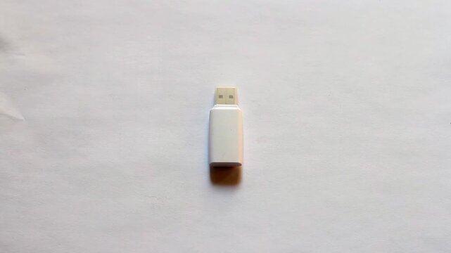 High angle view of a blank white USB flash drive lying on a clean white paper surface. Concept for digital data storage, backup, and technology.