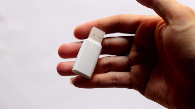 High angle view of a blank white USB flash drive lying on a clean white paper surface. Concept for digital data storage, backup, and technology.