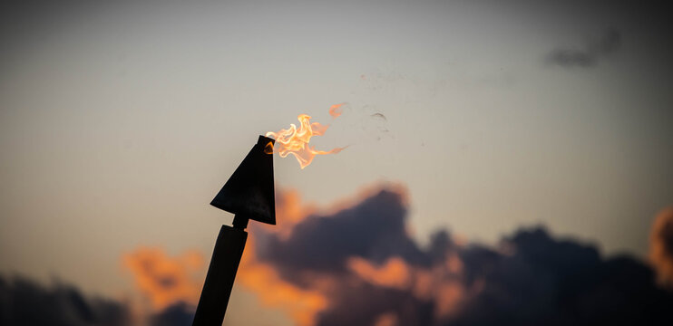 silhouette of a burning tiki torch against a lightly cloud sunset, Hawaii 