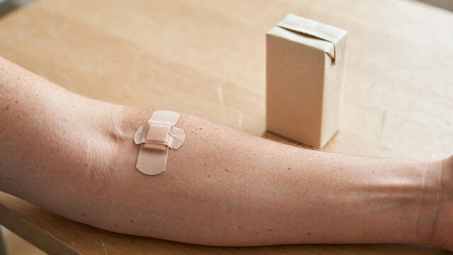 Close-up of blood donor arm with plaster bandage and juice box on table