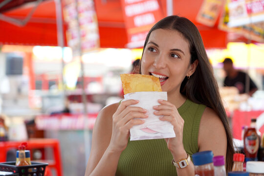 Young tourist woman eats a Pastel at a fair in the Japanese district of the metropolis of S&atilde;o Paulo, Brazil