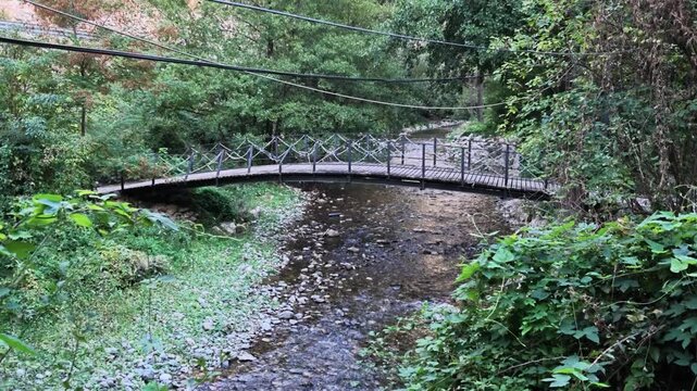 prizren small wooden suspension bridge spanning a shallow, rocky stream surrounded by dense green foliage, bazhderhane
