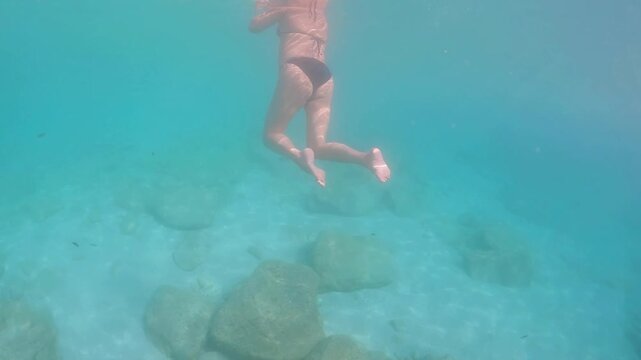 Underwater view of a woman swimming in clear turquoise sea water with small fish near Petani beach in Kefalonia island, Greece