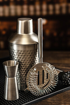 Stainless steel shaker jigger strainer on black mat. Blurred bar background