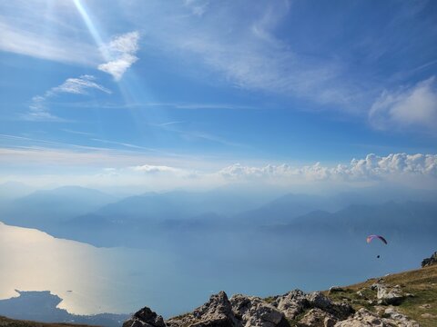 Paraglider over hazy Lake Garda and layered mountains from Monte Baldo