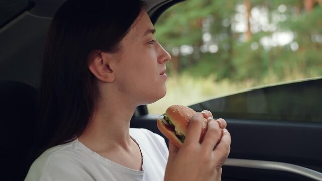 woman girl eating burger car, happy person, Hungry passenger, Eating delicious burger, Peaceful forest background, Calm lunch break, Road trip food, Sitting in backseat, Casual outfit, Concentrated