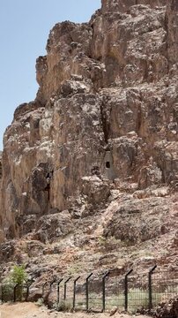 Panning shot of a rugged rocky desert mountain cliff behind a wire fence.