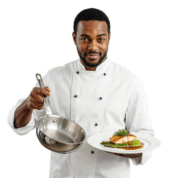 A smiling male chef in a white uniform presents a plate of gourmet salmon with asparagus and holds a frying pan.