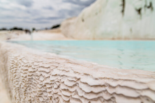 Macro close-up of white travertine mineral deposit edge with blue thermal water pool at Pamukkale