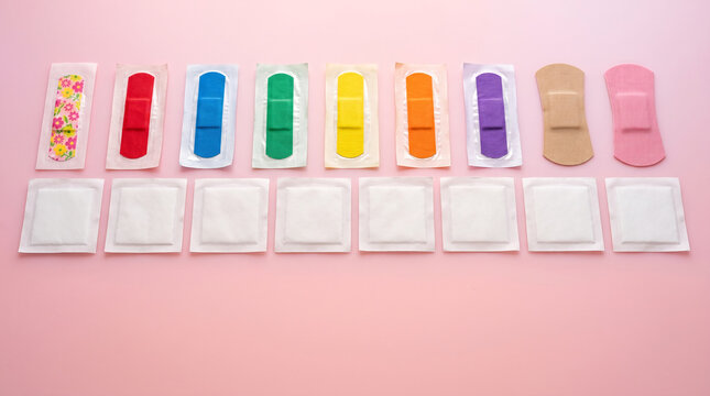 Assorted colorful adhesive bandages and sterile gauze pads arranged on pink background