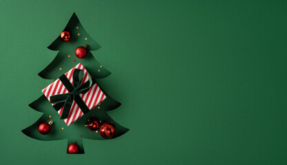 Fototapeta premium Minimal Christmas tree cutout with striped present and red ornaments for Merry Christmas and Happy New Year on banner green background